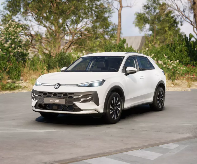 Gelber VW T-Roc SUV, Frontansicht, geparkt auf Asphalt, umgeben von Bäumen und Sträuchern.