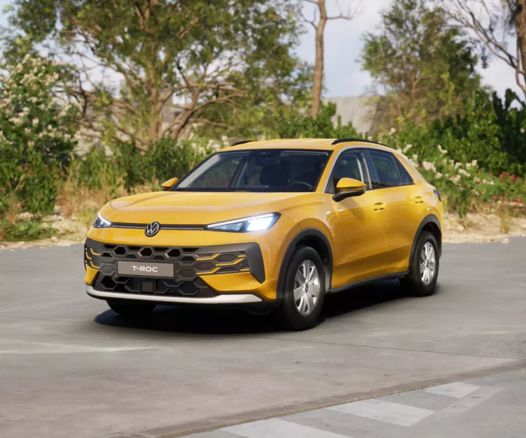 Gelber VW T-Roc SUV, Frontansicht, geparkt auf Asphalt, umgeben von Bäumen und Sträuchern.