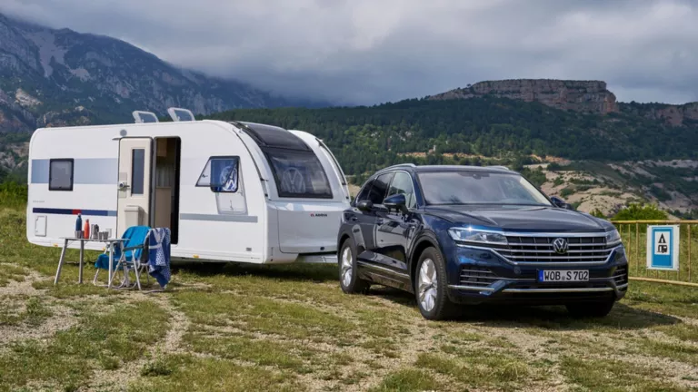 Ein Wohnwagen ist an die Kugelkopfkupplung / an die Anhängerkupplung eines Volkswagens angehängt.