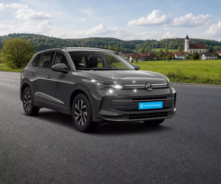Ein VW Tiguan steht auf einer Straße. Im Hintergrund sieht man die Berge und ein kleines Dorf.