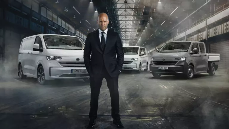 Jason Statham steht vor dem neuen Transporter Kastenwagen, dem neuen Transporter Kombi und dem neuen Transporter Pritschenwagen in einer Lagerhalle.