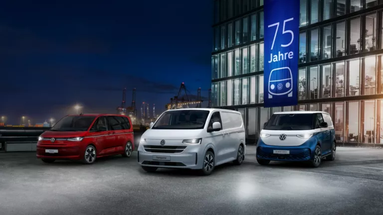 Ein VW Caddy, California, ID. Buzz Cargo, Multivan und Transporter Kastenwagen stehen bei Nacht vor einem Bürogebäude im Hafen.