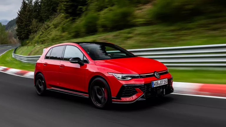 Ein roter Volkswagen Golf GTI fährt schnell auf einer Rennstrecke durch eine grüne, bewaldete Landschaft.