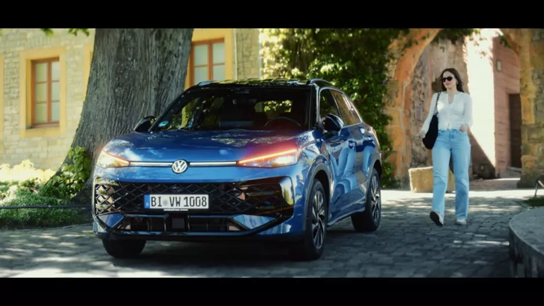 Gelber VW T-Roc SUV, Frontansicht, geparkt auf Asphalt, umgeben von Bäumen und Sträuchern.