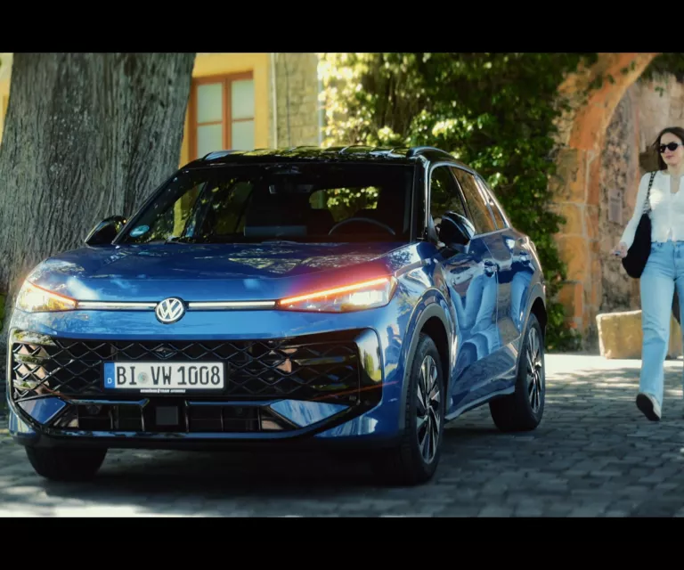 Gelber VW T-Roc SUV, Frontansicht, geparkt auf Asphalt, umgeben von Bäumen und Sträuchern.