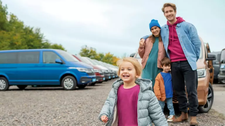 Familie mit zwei Kindern steht auf einem Parkplatz mit mehreren geparkten Transportern