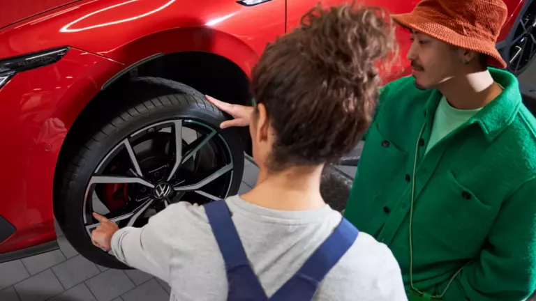 Una mujer mecánica y u hombre mirando la rueda de un Volkswagen rojo elevado