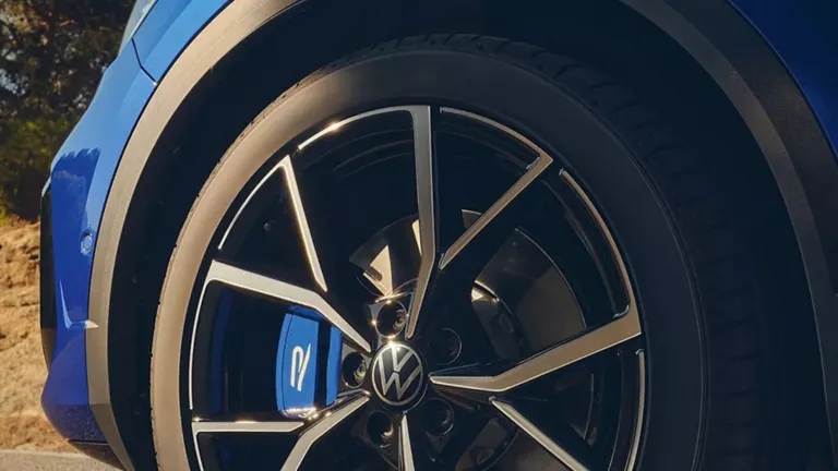 Nahaufnahme eines schwarzen und silbernen Volkswagen-Felgens mit blauem Bremssattel an einem blauen Auto