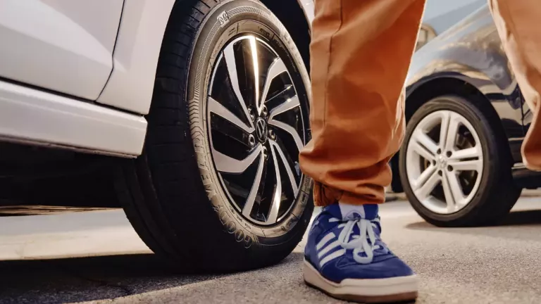 Nahaufnahme von Person mit blauen Turnschuhen vor zwei VW Autos – Räder und Reifen im Fokus