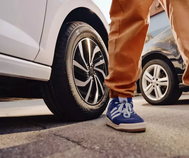 Nahaufnahme von Person mit blauen Turnschuhen vor zwei VW Autos – Räder und Reifen im Fokus