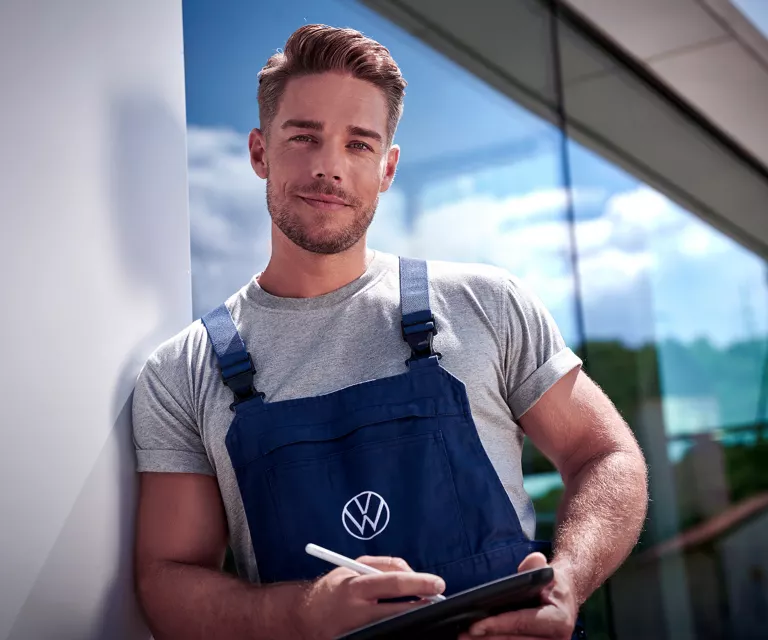 Ein VW Mitarbeiter in Arbeitskleidung steht vor einem Volkswagen Autohaus