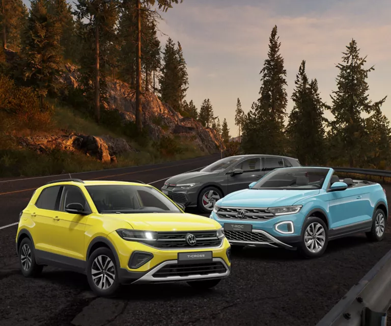 Ein gelber VW T-Cross, ein blauer VW T-Roc Cabriolet und ein grauer VW Golf GTI stehen auf einer Bergstraße bei Sonnenuntergang.