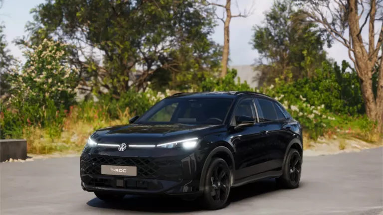 Schwarzer VW T-Roc SUV, Frontansicht, geparkt auf Asphalt, umgeben von Bäumen und Sträuchern.