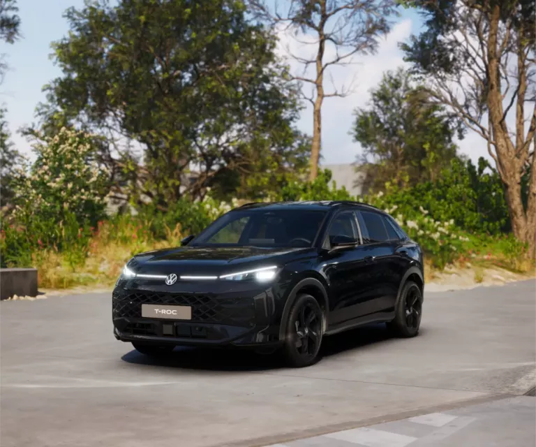 Schwarzer VW T-Roc SUV, Frontansicht, geparkt auf Asphalt, umgeben von Bäumen und Sträuchern.