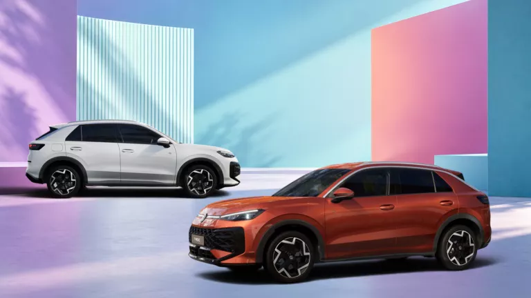 Ein weißer und ein roter T-Roc R-Line, stehen vor pastellfarbenen geometrischen Wänden in einem hellen Raum.