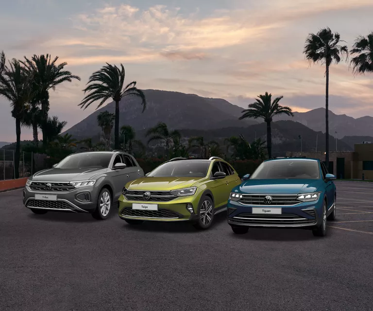 Der T-Roc, Taigo und Tiguan stehen auf einem Platz mit einem Berg im Hintergund.