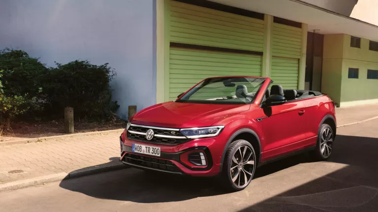Ein rotes T-Roc Cabriolet parkt am Straßenrand mit geöffnetem Dach.
