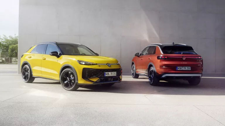 Ein gelber VW T-Roc R-Line und ein roter VW T-Roc Style stehen nebeneinander vor einem modernen Gebäude.