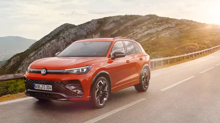Ein roter VW Tiguan fährt auf einer Straße mit Bergen im Hintergrund.