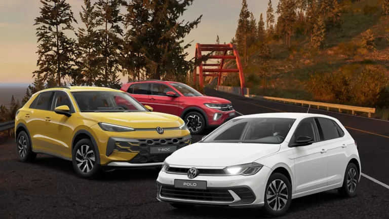 Drei VW-Modelle in Gelb, Weiß und Rot parken seitlich auf der straße mit herbstlichen hintergrund. 