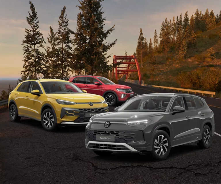 Drei geparkte VW-SUV-Modelle in Gelb, Rot und Grau am Straßenrand, mit Herbstbäumen im Hintergrund.