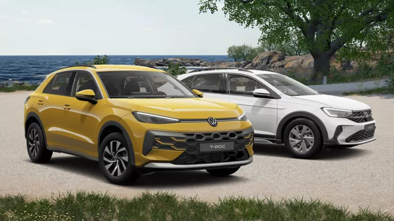 VW T-Roc und VW Taigo stehen an einem Sandstrand am Meer, mit Gras im Vordergrund und Bäumen im Hintergrund