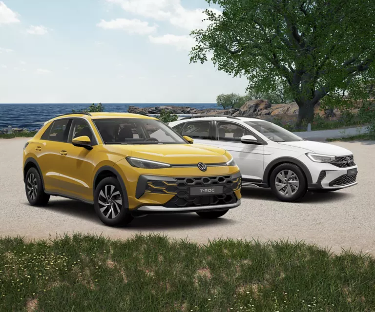 VW T-Roc und VW Taigo stehen an einem Sandstrand am Meer, mit Gras im Vordergrund und Bäumen im Hintergrund