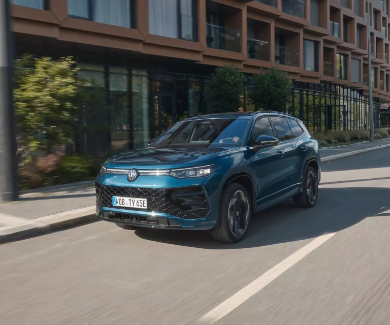 Gelber Volkswagen T-Roc und grauer Tiguan vor Kirschblüten auf einem Parkplatz.