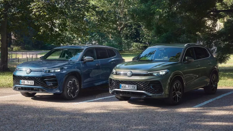 Zwei geparkte VW SUV-Modelle in Blau und Grau auf gepflastertem Parkplatz vor Bäumen.