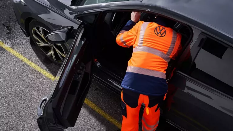 Wir sehen aus der Vogelperspektive einen VW Mitarbeiter mit oragener Signalkleidung der sich auf der Fahrerseite in ein Fahrzeug beugt.