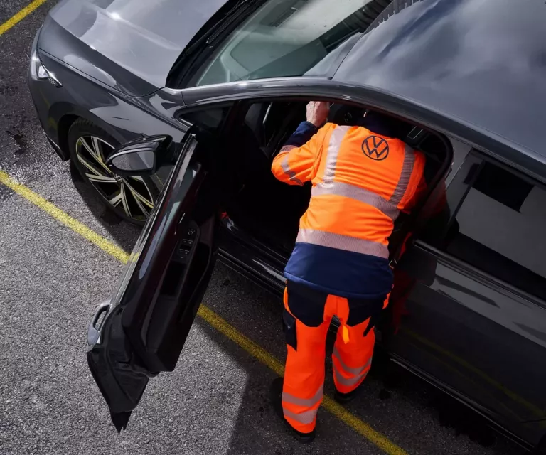 Wir sehen aus der Vogelperspektive einen VW Mitarbeiter mit oragener Signalkleidung der sich auf der Fahrerseite in ein Fahrzeug beugt.