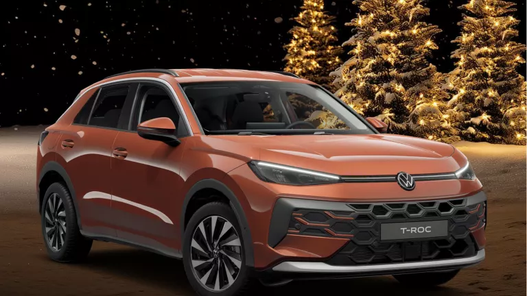 Roter VW T-Roc in winterlicher Umgebung mit drei leuchtenden Tannenbäumen im Hintergrund.
