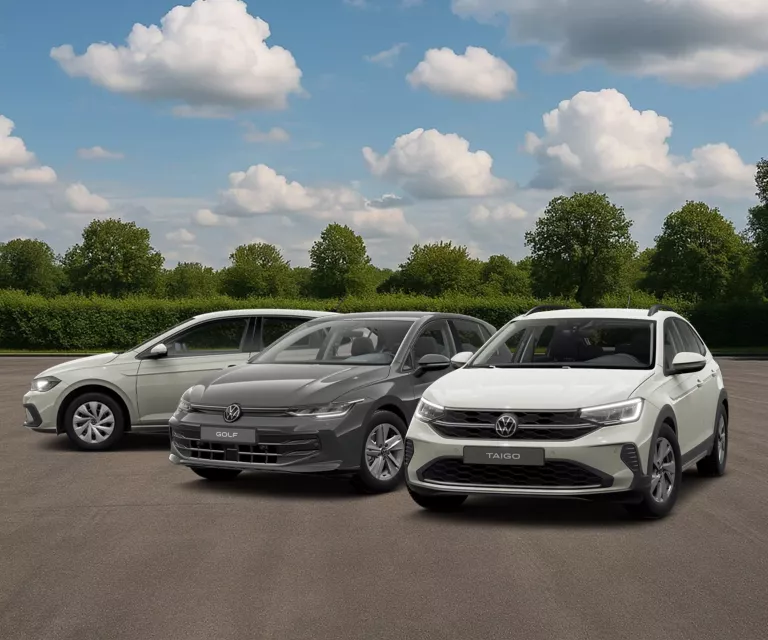 Drei VW-Modelle auf Asphalt, im Hintergrund grüne Hecken, Bäume und blauer Himmel