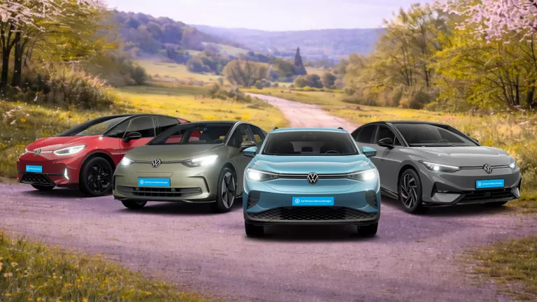 Vier Volkswagen-Elektroautos stehen auf einem ländlichen Weg vor einer bewaldeten Hügellandschaft