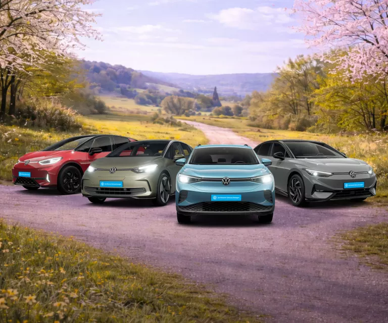 Vier Volkswagen-Elektroautos stehen auf einem ländlichen Weg vor einer bewaldeten Hügellandschaft