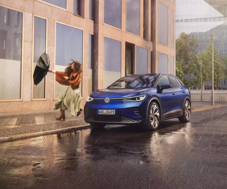 Bild zeigt einen ID. 4. Er steht im Regen vor einem Gebäude. Daneben steht eine Frau mit einem Regenschirm.