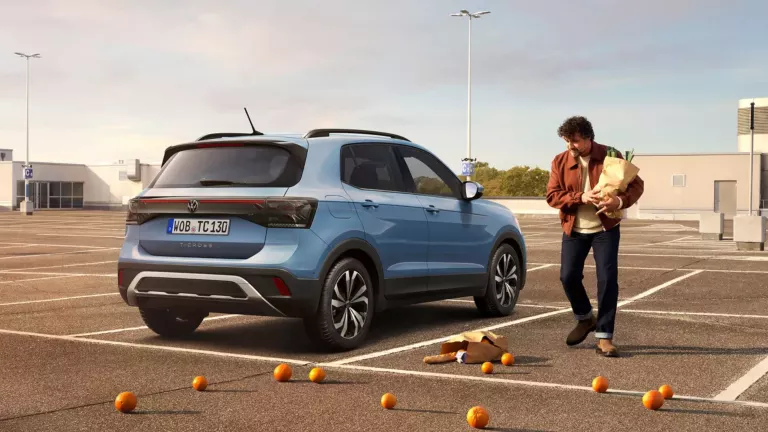 Ein blauer T-Cross steht auf einem Parkdeck. Neben ihm steht ein Mann mit einer Einkaufstasche, aus der Orangen herausfallen.