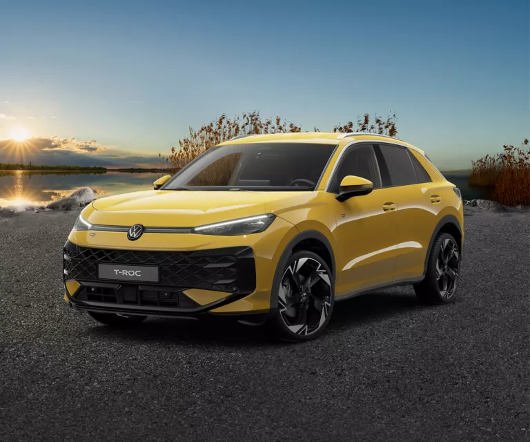 Frontale Ansicht eines gelben VW T-Roc, der auf Asphalt steht, vor Schilf und einem See.
