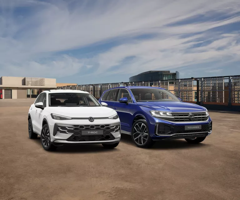 Ein dunkelblauer Touareg „FINAL EDITION“ parkt an einem Seitenstreifen vor einem futuristischen Gebäude. Im Hintergrund sind weitere Gebäude sowie grüne Bäume zu erkennen.