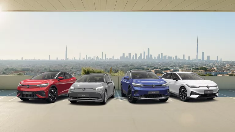 Vier VW-Elektroautos in Rot, Grau, Blau und Weiß stehen nebeneinander vor einer Stadtlandschaft mit hohen Gebäuden.