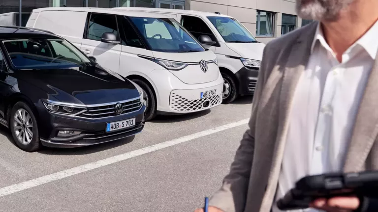 Ein Mann mit Tablett steht vor einem Volkswagen Autohaus