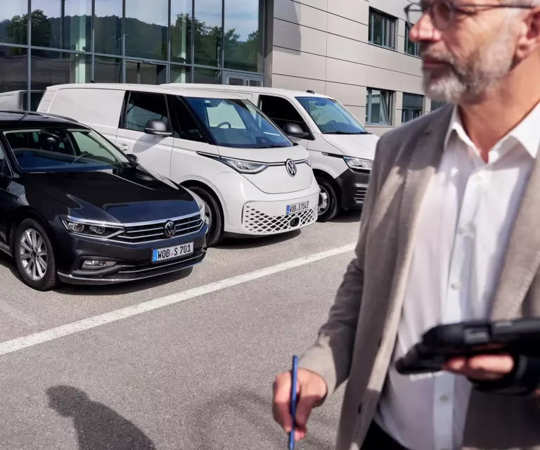Ein Mann mit Tablett steht vor einem Volkswagen Autohaus
