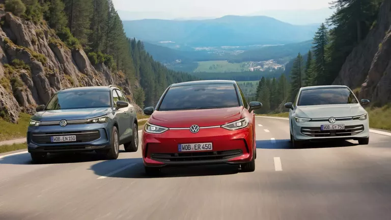 Drei VW-Fahrzeuge fahren nebeneinander auf einer kurvigen Bergstraße. In der Mitte ein roter VW ID.3, links ein grauer VW Golf und rechts ein silberner VW Tiguan