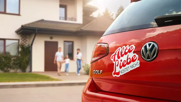 Roter VW Golf mit Aufkleber 'Alte Liebe kostet nicht' am Heck, Familie läuft auf Haus zu