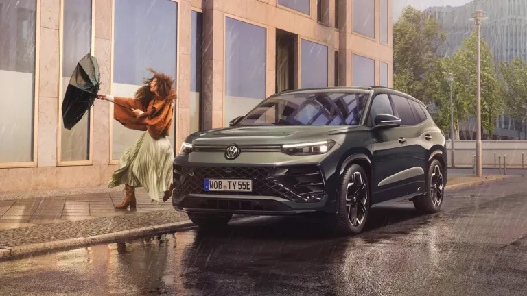 Ein grüner Tayron steht an der Straße. Neben ihm steht eine Frau mit einem Regenschirm im Wind und Regen.