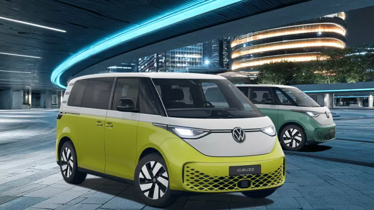 Zwei VW ID. Buzz Elektro-Vans in gelb-weiß und grün-weiß vor moderner, beleuchteter Architektur bei Nacht.
