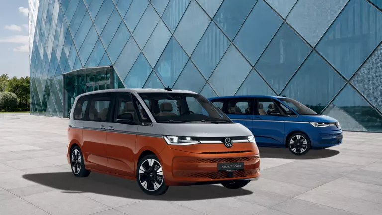 Zwei VW Multivan vor einem modernen Glasgebäude, ein orange-schwarzer und ein blau-schwarzer Van.