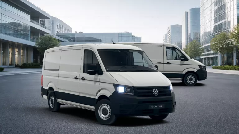 Zwei weiße VW Crafter Transporter vor modernen Glasgebäuden auf einem Parkplatz.