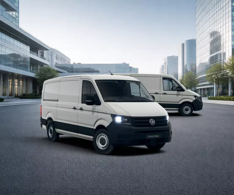 Zwei weiße VW Crafter Transporter vor modernen Glasgebäuden auf einem Parkplatz.