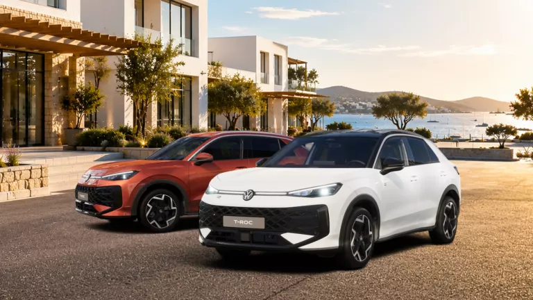 Zwei moderne VW T-Roc SUV, ein weißes und ein rotes, stehen vor einem modernen Haus mit Meerblick bei Sonnenuntergang.